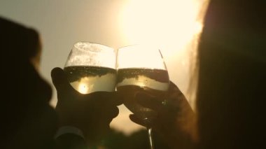 Şampanya parıldıyor ve güneşte köpükler. İki aşık ile köpüklü şarap şarap gözlük günbatımı arka plan üzerinde tutarak. portre. seven çift, takım çalışması. başarı ve zafer kutluyor. Ağır çekim