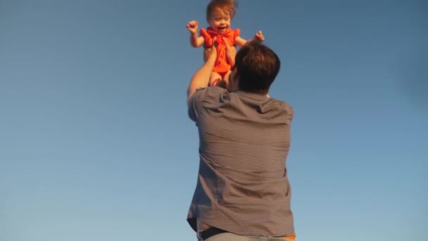 O pai atira a filha para o céu azul. O pai brinca com uma criança pequena. família feliz jogando à noite contra o céu. O pai vomita o bebé, o miúdo sorri. Movimento lento. família feliz — Vídeo de Stock