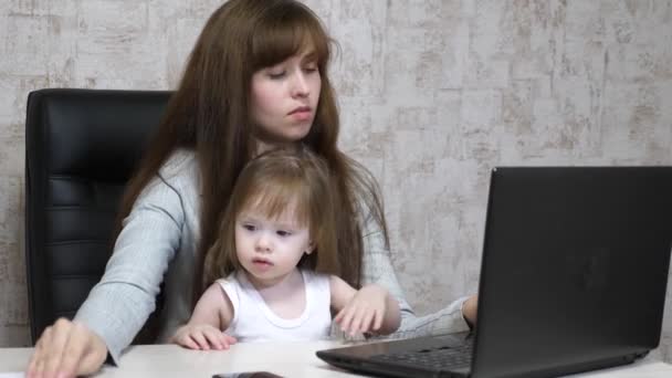 Mãe trabalhadora com a filha na mesa. Mulher ocupada trabalhando em laptop com bebê em mãos. Mãe trabalhando com belo bebê a mãos em casa aconchegante. Trabalho freelancer feminino. Maternidade moderna — Vídeo de Stock