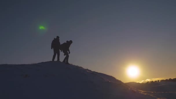 Z vrcholku kopce sestoupí cestovatelé. Turisté sejdou po zasněženém svahu při západu slunce. Alpenisté cestují, pěší turistiku. cestovatel a spolucestující. — Stock video