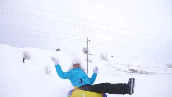 Glückliches Mädchen gleitet auf Schlitten durch den Schnee, schöne junge Frau gleitet auf einem aufblasbaren Schneeröhrchen im Schnee hinunter und winkt mit der Hand. Mädchen spielt im Park für die Weihnachtsfeiertage im Winter — Stockfoto
