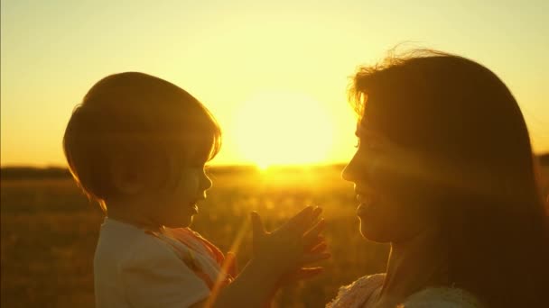 Moeder speelt met haar kleine dochter in het park bij zonsondergang. kind zit in de armen van de moeder. Gelukkige Familiewandelingen in het voorjaar. Mama en baby in de zon. Slow Motion. concept van gelukkige familie en kinderjaren. — Stockvideo