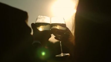 Şampanya parıldıyor ve güneşte köpükler. İki aşık ile köpüklü şarap şarap gözlük günbatımı arka plan üzerinde tutarak. portre. seven çift, takım çalışması. başarı ve zafer kutluyor. Ağır çekim