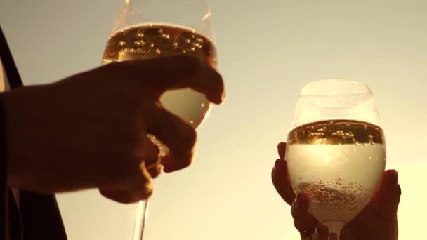 Champagner funkelt und schäumt in der Sonne. Verliebte Paare halten Weingläser mit Sekt vor dem Hintergrund des Sonnenuntergangs. Nahaufnahme. Teamwork eines liebenden Paares. Erfolg und Sieg feiern. Zeitlupe — Stockvideo