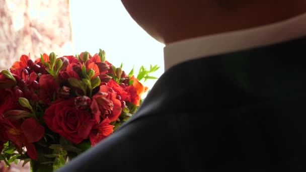 Pan młody z kwiatami. piękny bukiet czerwonych róż w rękach mężczyzny w marynarce i białej koszulce. Zbliżenie. piękne kwiaty w rękach człowieka prezent dla ukochanej kobiety. — Wideo stockowe