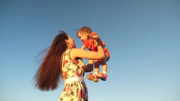 Mamma kastar sin dotter upp till himlen. mor leker med ett litet barn mot en blå himmel. lycklig familj spelar på kvällen mot himlen. mamma kastar upp barnet, barn leenden. slow motion Filmning. — Stockfoto