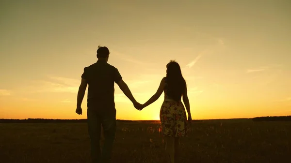 Jeune couple amoureux marchant sur le terrain en se tenant la main. Fille et homme vont au coucher du soleil. joyeuses promenades en famille dans le parc en été aux rayons du soleil. concept de famille heureuse — Photo