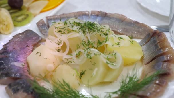 Servertisch in einem Teller gesalzenen Fisch mit Gemüse im Restaurant bestreut. leckeres Essen auf dem Tisch. Hering in Scheiben geschnitten auf einem Teller mit gekochten Kartoffeln mit Dill bestreut. All inclusive — Stockvideo