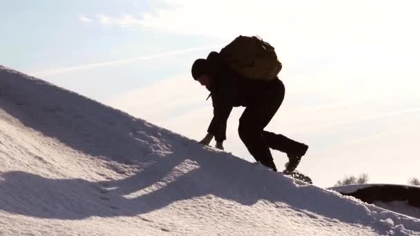 Hombre alpinista se mueve a la cima de su éxito. Escalador sube montaña nevada en rayos de sol brillante. el viajero se regocija en su victoria y levanta sus manos contra el cielo en la cima de la montaña — Vídeo de stock