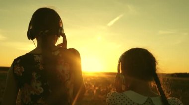 kız kardeşler birlikte müzik dinlerler. Mutlu genç kızlar parkta güzel gün batımı ışınları müzik ve dans dinlerken. sıcak bir günbatımı ışınları altında uçuş kulaklık çocuklar.