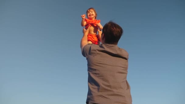 Far kastar sin dotter upp till blå himmel. Pappa leker med ett litet barn i armarna mot himlen. lycklig familj spelar på kvällen mot himlen. far kastar upp Happy baby, baby Smiles — Stockvideo