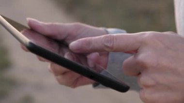 kızın parmak dokunmatik ekran tablet, smartphone. yakın çekim. Eller bir tablet tutarak ve e-postaları parkta günbatımında kontrol. Kızlar el bir mobil ileti smartphone ekranında yazdırır..