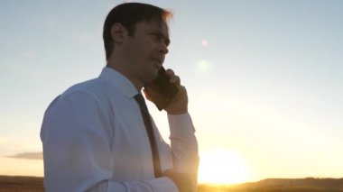 gün batımında parkta bir tablet ile kravat adam. gökyüzüne karşı bir akıllı telefon konuşuyor işadamı. akıllı telefonda mobil mesaj konuşuyor. bir cep telefonu ile bir ülke yolda işadamı