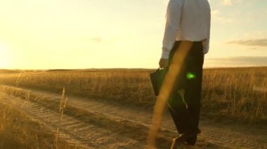 iş adamı elinde bir çanta ile köy yolunda devam ediyor. Girişimci bir kırsal bölgede çalışıyor. gün batımında akşamları toprağını bir çiftçi olup olmadığını denetler. tarıma dayalı işletme kavramı.