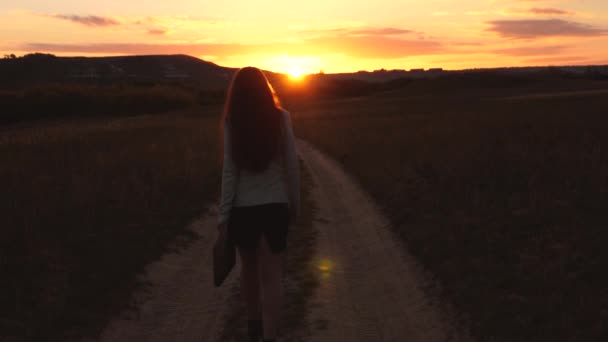 太陽の手でブリーフケースの国の道路に沿って歩くセクシーなビジネスウーマンは日没でゆらめきます。田舎で働くセクシーなビジネス女性。美しい少女は、田舎を旅します。. — ストック動画