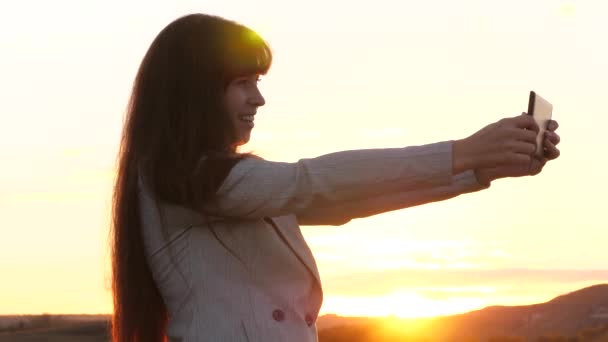 Beautiful business woman travels and takes a selfie photo using a mobile smartphone against the backdrop of the sunset. Girl tourist in the field makes selfie with tablet. concept of tourism — Stock Video