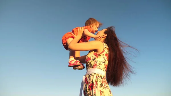 Madre getta sua figlia in cielo blu. riprese al rallentatore. Mamma gioca con un bambino piccolo tra le braccia contro il cielo. famiglia felice che gioca in serata contro il cielo. mamma vomita bambino, bambino sorride — Foto Stock