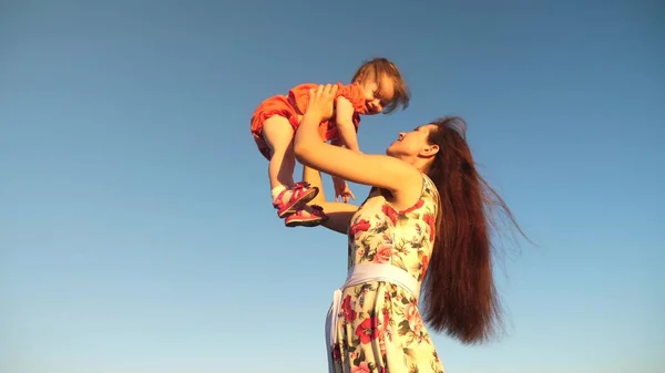 Mère jeter sa fille vers le haut à blu ciel. tournage au ralenti. Maman joue avec un petit enfant dans ses bras contre le ciel. famille heureuse jouant en soirée contre le ciel. mère vomit bébé, bébé sourit — Photo