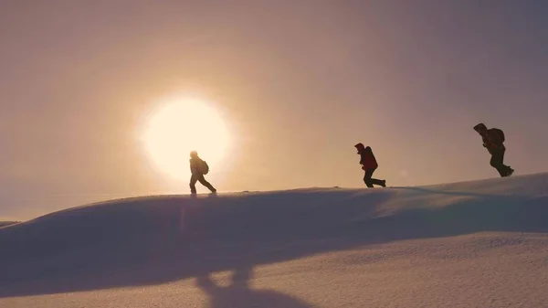 Команда альпинистов следует друг за другом вдоль снежного хребта в лучах желтого зонта. работа в команде туристов, преодоление трудностей для перехода к победе и успеху. Силуэты путешественников идут к победе — стоковое фото