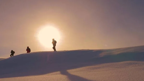 Équipe d'alpinistes se suivent le long de la crête des neiges dans les rayons de soleil jaune. travailler en équipe de touristes, surmonter les difficultés de passer à la victoire et le succès. silhouettes de voyageurs vont à la victoire — Photo