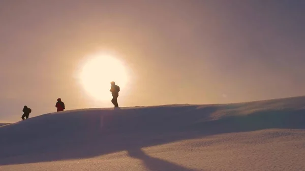 登山者のチームは黄色の sunt の光線で雪尾根に沿ってお互いに従ってください。勝利と成功に移動に困難を克服し、観光客のチームで働いてください。勝利への旅行者のシルエット — ストック写真