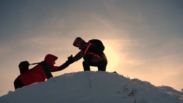 チームワークと勝利。観光客は丘の頂上に上がる友人に手を拡張します。カマンダで雪の山の仕事で冬の登山者は、丘を登るのに役立ちます。スポーツツーリズムのコンセプト. — ストック写真