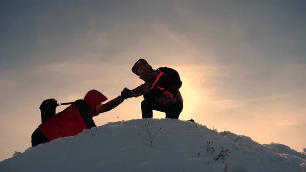 チームワークと勝利。観光客は丘の頂上に上がる友人に手を拡張します。カマンダで雪の山の仕事で冬の登山者は、丘を登るのに役立ちます。スポーツツーリズムのコンセプト. — ストック写真