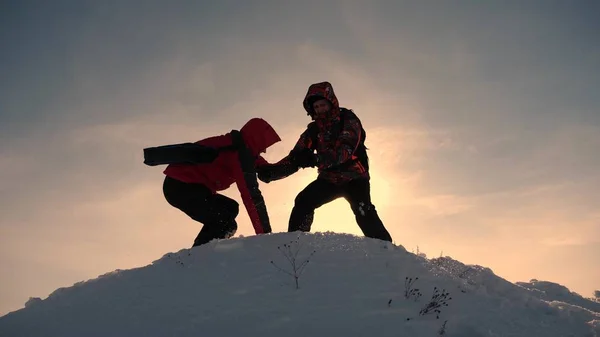 Týmovou práci a vítězství. Turisté táhnou ruku k příteli, který stoupá na vrchol kopce. Horolezci v zimě na zasněžené horské práci v Kamandě, kteří pomáhají šplhat na kopec. koncepce sportovního turismu. — Stock fotografie