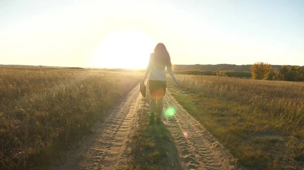 business woman walking along a country road with a briefcase in her hand. sexy business woman girl working in rural area. woman farmer inspects land at sunset. agricultural business concept.