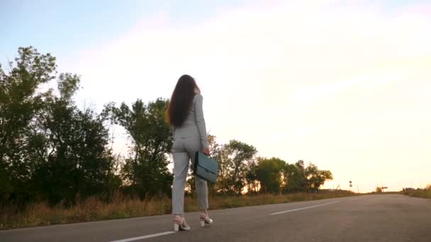 Mooie vrouw die door de straat loopt tegen een blauwe hemel. zakenvrouw loopt op de weg met een zwarte aktetas in haar hand. Achteraanzicht. sexy zakenvrouw met lange benen lopen langs de weg. — Stockvideo