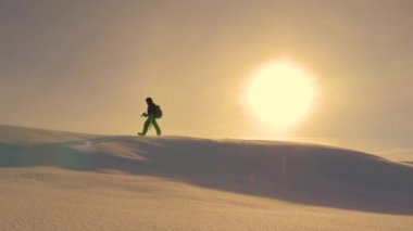 kamera ve tripod ile dağcı bir holom üstünde karda yürüyor. kışın fotoğrafçı gezgin sarı günbatımı ışınları karlı sırta gider.