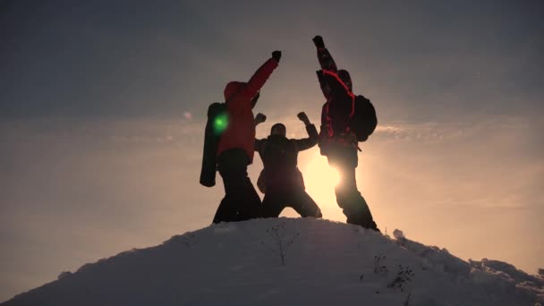 Los viajeros llegan a la cima de la colina nevada y se regocijan por la victoria contra el telón de fondo de una puesta de sol amarilla. Turistas trabajo en equipo y victoria. trabajo en equipo alpinista de personas en condiciones difíciles. Movimiento lento — Vídeos de Stock