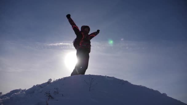 여행자는 눈 덮인 언덕 꼭대기에서 승리를 기뻐하며, 행복한 사람인 팔을 점프하고 흔들며 기뻐합니다. 관광객은 태양에 의해 조명 산에서 내려온다. 슬로우 모션 — 비디오