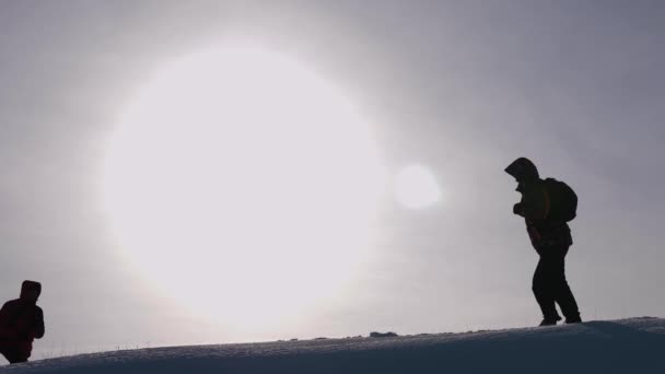 Dois viajantes se alegram em sua vitória no topo de uma colina nevada, pulando e acenando com as mãos, homens felizes. turistas no fundo de grande sol brilhante. alpinistas do trabalho em equipa — Vídeo de Stock