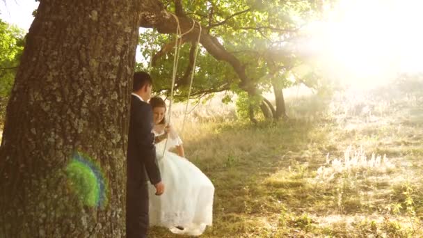 Ragazzo e ragazza oscillano su un ramo di una quercia nella foresta estiva. Lo sposo felice che oscilla su un'oscillazione la sposa nel parco in estate. felice concetto di famiglia. lavoro di squadra di una coppia innamorata . — Video Stock