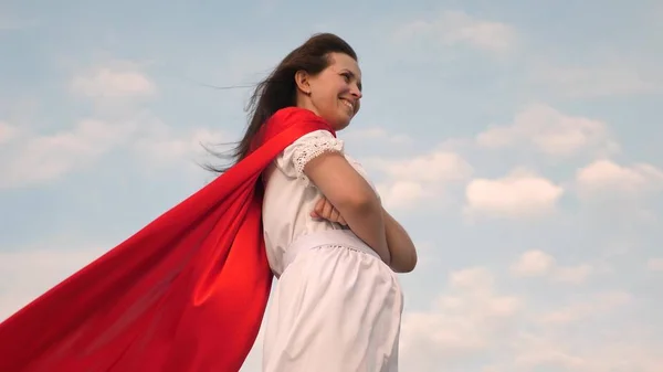 Menina super-herói em pé no campo com um manto vermelho, camuflando com o vento. close-up. menina sonha em se tornar um super-herói. menina em uma expressão de sonho capa vermelha — Fotografia de Stock