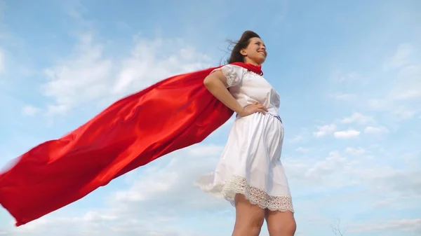 Sexy super-herói menina de pé no campo em um manto vermelho, vagueando camuflagem no vento. menina sonha em se tornar um super-herói. Movimento lento. menina em uma expressão de sonho capa vermelha — Fotografia de Stock