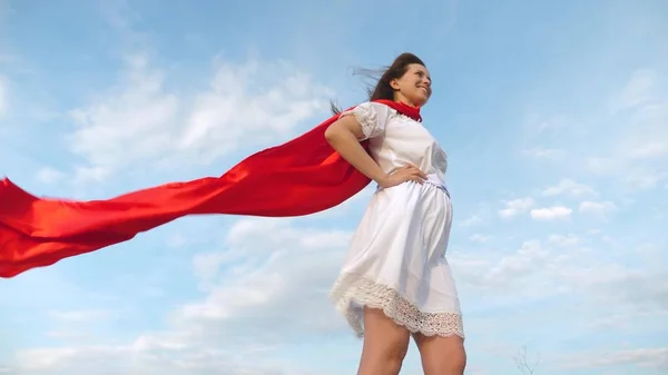 Sexy super-herói menina de pé no campo em um manto vermelho, vagueando camuflagem no vento. menina sonha em se tornar um super-herói. Movimento lento. menina em uma expressão de sonho capa vermelha — Fotografia de Stock