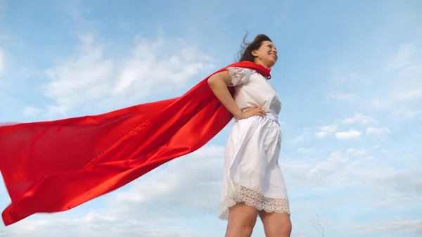 Sexy super-herói menina de pé no campo em um manto vermelho, vagueando camuflagem no vento. menina sonha em se tornar um super-herói. Movimento lento. menina em uma expressão de sonho capa vermelha — Fotografia de Stock