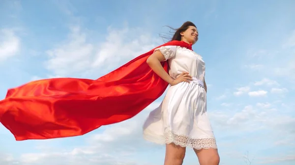 Sexy super-herói menina de pé no campo em um manto vermelho, vagueando camuflagem no vento. menina sonha em se tornar um super-herói. Movimento lento. menina em uma expressão de sonho capa vermelha — Fotografia de Stock