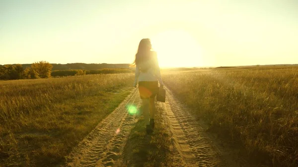 Donna d'affari che cammina lungo una strada di campagna con una valigetta in mano. sexy donna d'affari ragazza che lavora in zona rurale. donna contadina ispeziona la terra al tramonto. concetto di impresa agricola . — Foto Stock