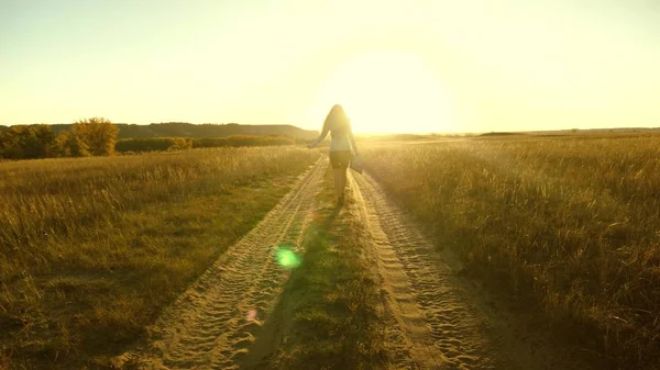 Femme d'affaires marchant le long d'une route de campagne avec une mallette à la main. sexy femme d'affaires fille travaillant dans la zone rurale. agricultrice inspecte les terres au coucher du soleil. concept d'entreprise agricole . — Photo