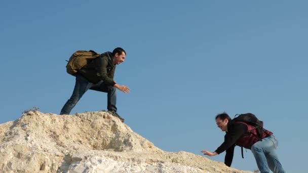 Two climbers climb one after another on white rock. teamwork of business people. tourists give hand to each other, climbing to top of the hill. team of male travelers goes to victory and success. — Stock Video