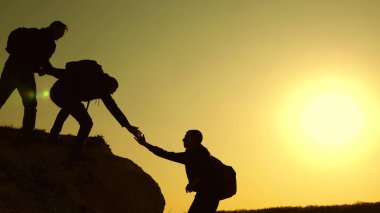 Dağcılar siluetler ellerini birbirlerine uzatır ve tepenin tepesine çıkarlar. gezginler kayaüzerinde birbiri ardına tırmanıyorlar. iş adamlarının takım çalışması. Bir grup işadamı.