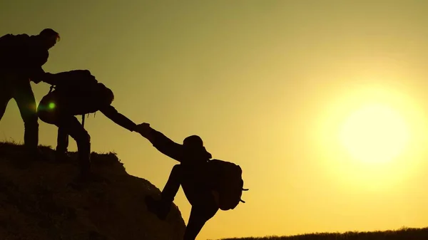 Dağcılar siluetler ellerini birbirlerine uzatır ve tepenin tepesine çıkarlar. gezginler kayaüzerinde birbiri ardına tırmanıyorlar. iş adamlarının takım çalışması. Bir grup işadamı.