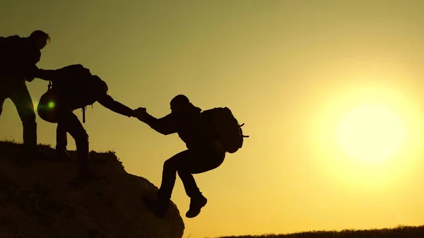 Dağcılar siluetler ellerini birbirlerine uzatır ve tepenin tepesine çıkarlar. gezginler kayaüzerinde birbiri ardına tırmanıyorlar. iş adamlarının takım çalışması. Bir grup işadamı.