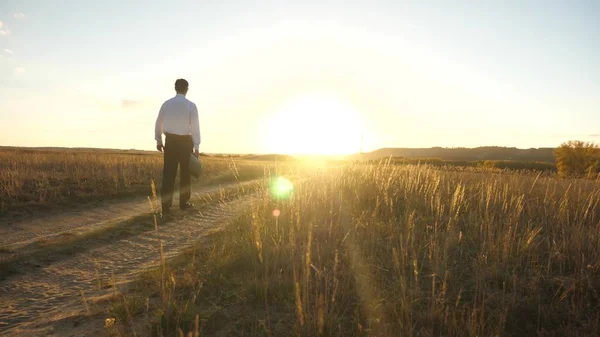 businessman in sunglasses goes down the country road with a briefcase in his hand. The entrepreneur works in a rural area. a farmer inspects the land at sunset. agricultural business concept.