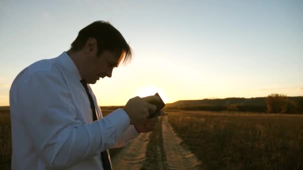 Geschäftsmann, der im Park in den warmen Strahlen des Sonnenuntergangs Tablet-Spiele spielt. Mann spielt Spiele auf dem Smartphone. glücklicher Mann in weißem Hemd und Krawatte spielt online auf Tablet. — Stockvideo