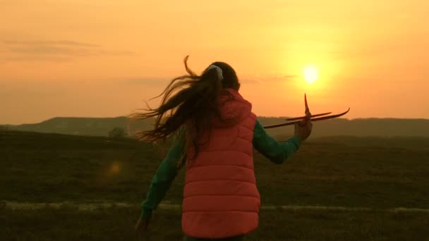 Un bambino gioca un aeroplano giocattolo. ragazza sogna di volare e diventare un pilota. Al rallentatore. Ragazza felice che corre con un aeroplano giocattolo sullo sfondo di un tramonto sul campo. concetto di una famiglia felice . — Video Stock