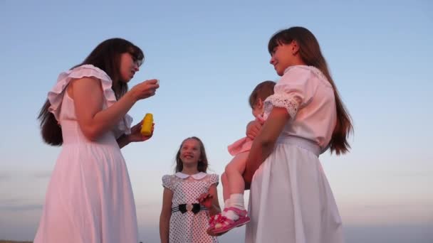 Daughters and mother are blowing bubbles in the park at sunset. Slow motion. Happy mother playing with children blowing soap bubbles. happy family concept. baby, sister and mom are playing in sun. — Stock Video